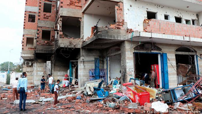 People stand amid debris at the site of a deadly car bomb attack close to a security checkpoint outside Aden’s international airport, in the neighborhood of Khormaksar