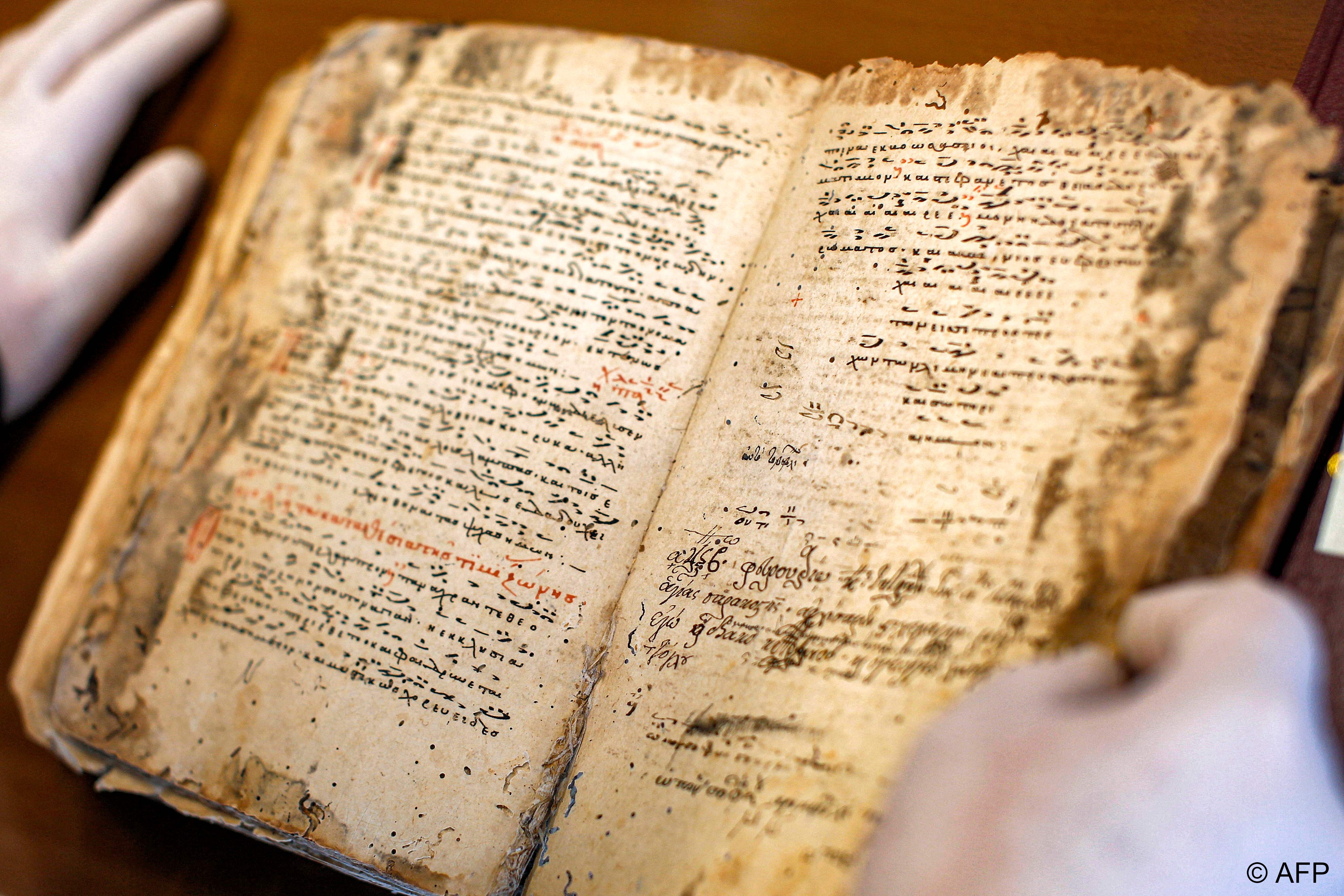 Greek Orthodox Priest Dimitrios Dimosthenous inspects a 14th-century-copy of a Byzantine chant manuscript showing the traditional notation at the Archbishop of Cyprus‘ archive in the capital Nicosia on 12 April 2022 (photo: Lisa Golden/AFP)