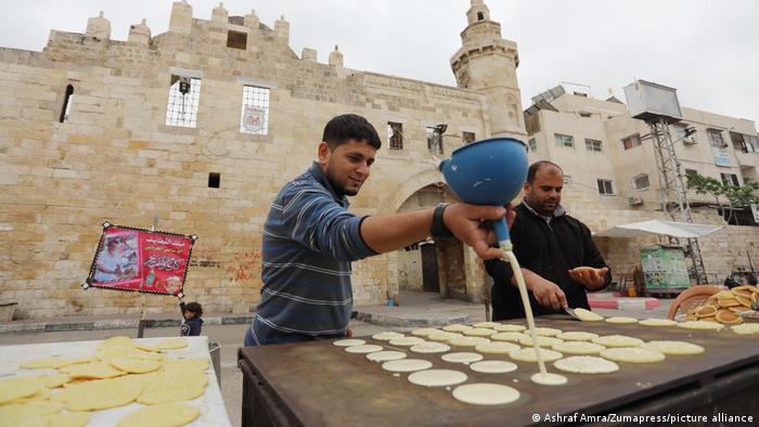 Zwei Männer vor einem historischen Stadttor backen Pfannkuchen auf einer großen Eisenplatte