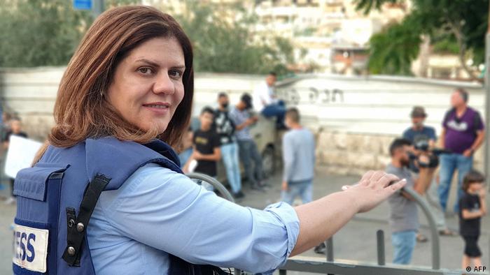 Shireen Abu Akleh wears a press vest, looking over her shoulder into camera