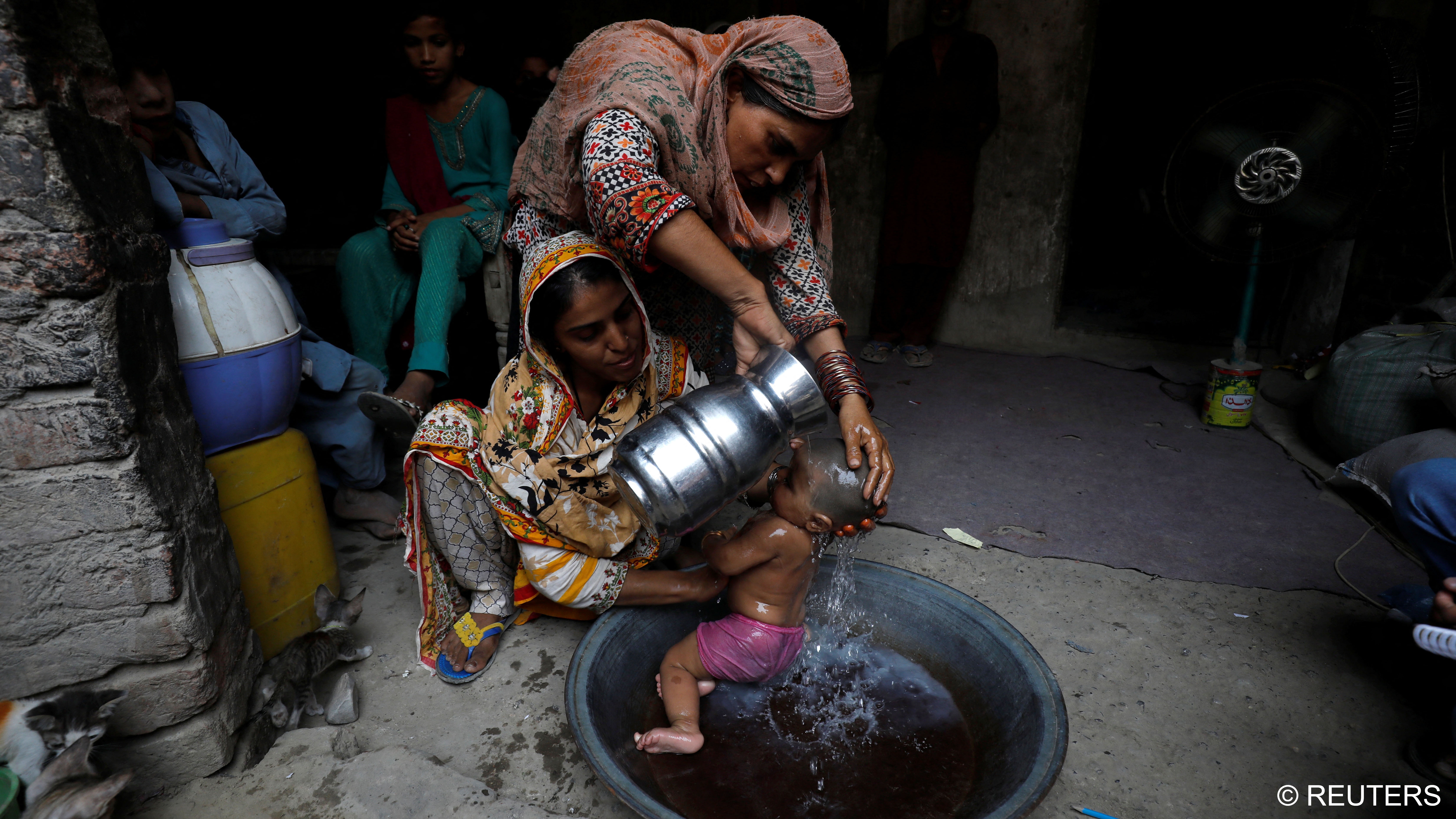 Rehmat, 30, helps Razia, 25, bathe her six-month-old daughter Tamanna (photo: Reuters/Akhtar Soomro)