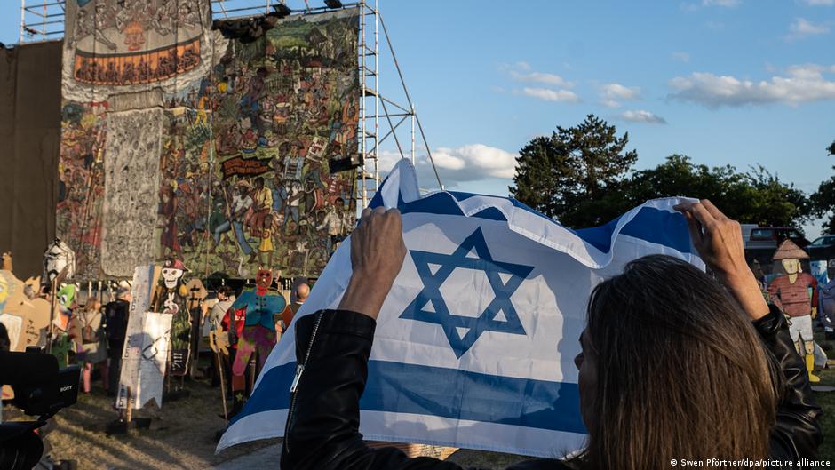 A woman holds up an Israel flag while the painting by Indonesian artist Taring is mounted. 