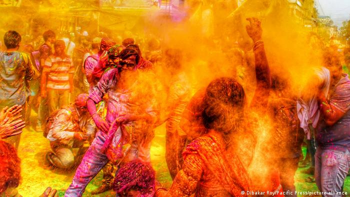 In a street, paint powder flies through the air, making the celebrating people hardly recognisable