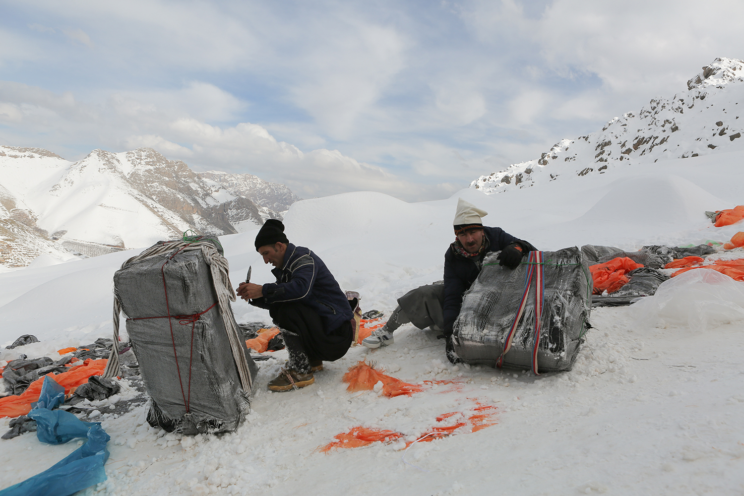 Two men squat to see to their packs surrounded by mountains (photo: Konstantin Novakovic)