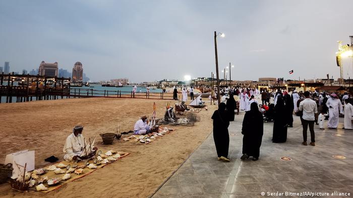 Strolling along the Corniche promenade: people walk along the beach as vendors sell things on the side of the road