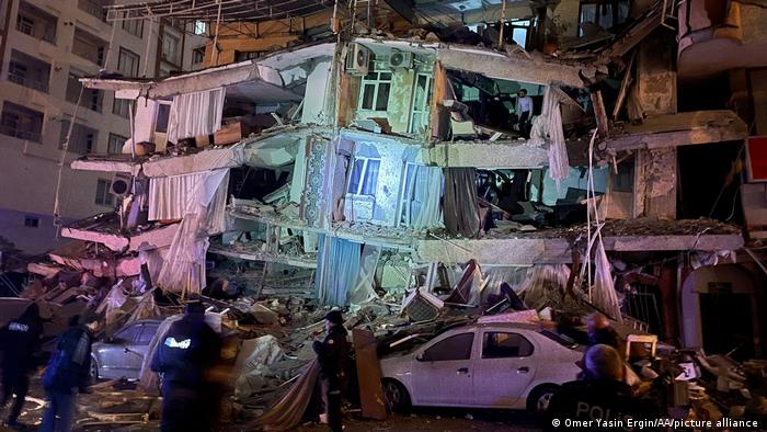 Collapsed residential building with completely destroyed barrel, inside and in front of it people