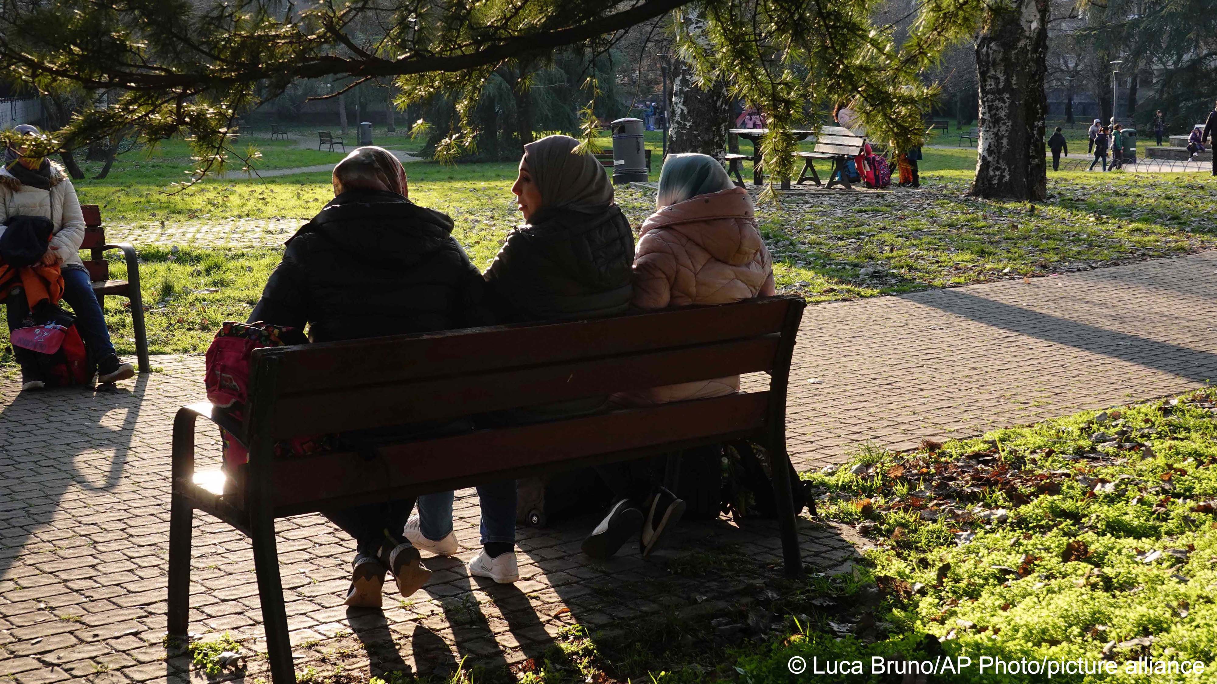 Pakistani women relax on a bench of a public park as their kids play outside a school at the Fiumicello district, populated heavily by migrants from India and Pakistan, in Brescia, northern Italy, 8 February 2023 (image: Luca Bruno/AP Photo/picture alliance) 