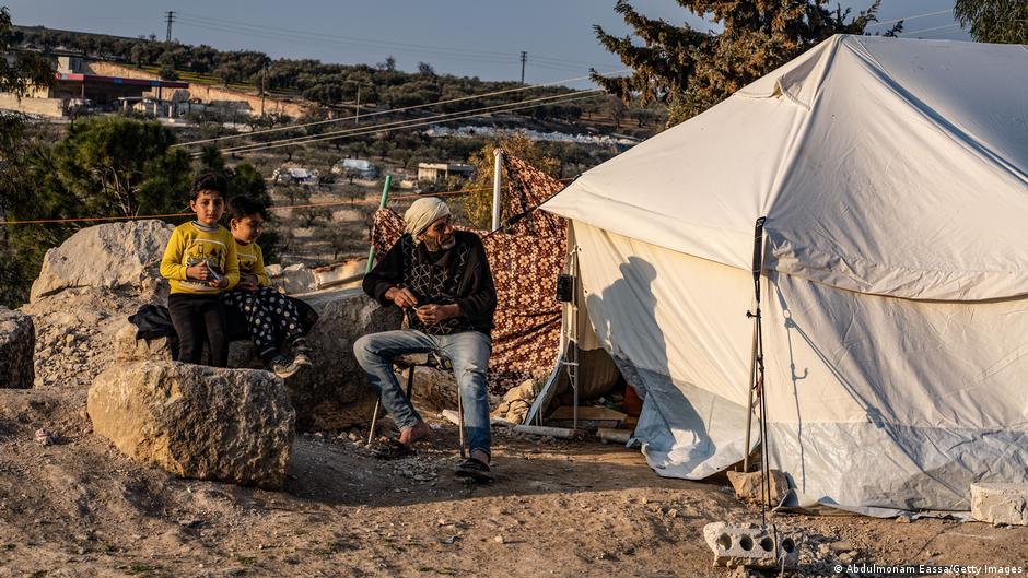 A man and two children sit outside a makeshift tent in a camp in Idlib (image: Abdulmonam Eassa/Getty Images)