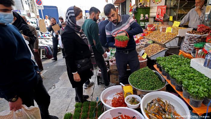 Men and a woman buying fresh fruit and herbs at a shop front.