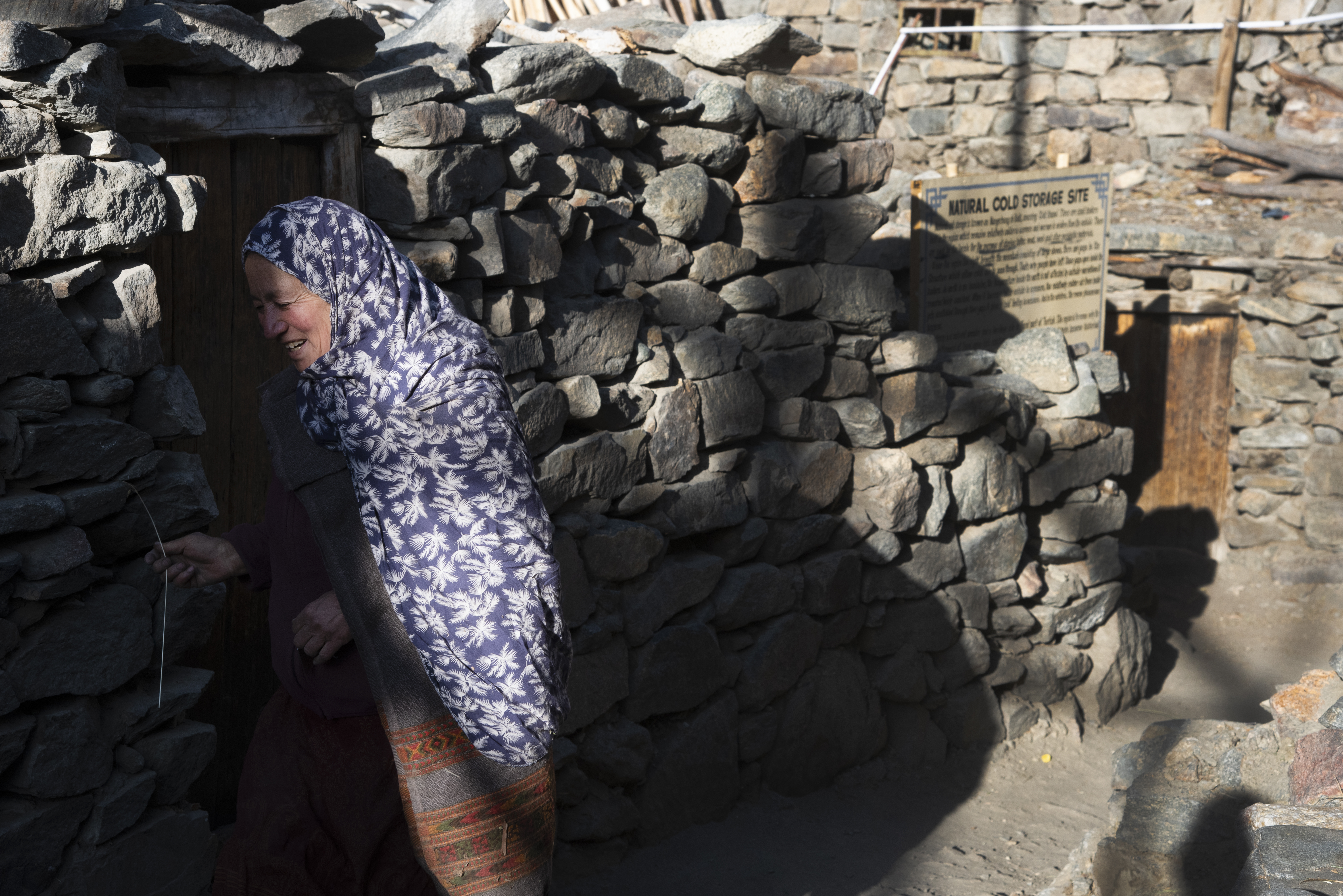 A woman smiles as she passes in front of an uneven stone wall, punctuated by doorways (image: Sugato Mukherjee)