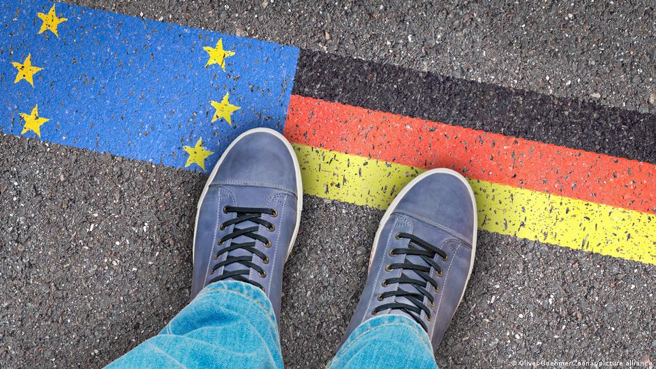 Ein Mann steht auf dem Asphalt, auf dem eine deutsche Flagge und die europäische Flagge aufgemalt ist (Foto: Oliver Boehmer/Zoonar/picture alliance)