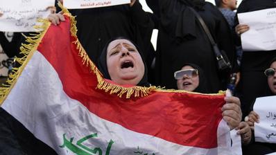 Irakische Frauen demonstrieren, darunter eine Frau, die die irakische Flagge hält (Foto: Picture Alliance/AP | H. Mizban)