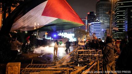 A man waves a Palestinian flag and others clash with anti riot policemen outside the Israeli consulate during a protest to show solidarity with Palestinians, Istanbul, Turkey, 18 October 2023