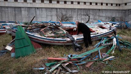 A man peers into a rickety wooden boat on dry land