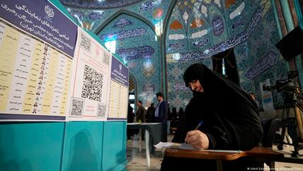 A woman holds a pen in her hand as she looks at a ballot paper at a polling station in Iran