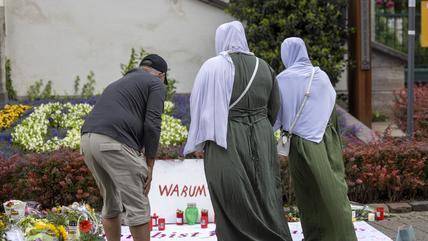 Ein Mann und zwei Frauen mit Kopftuch stehen vor einer Gedenktafel für die Opfer des Messerangriffs in Solingen.