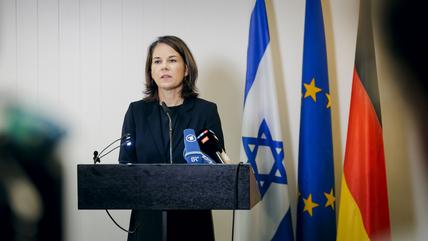 Baerbock makes a statement in front of an Israeli flag, a European flag and a German flag.