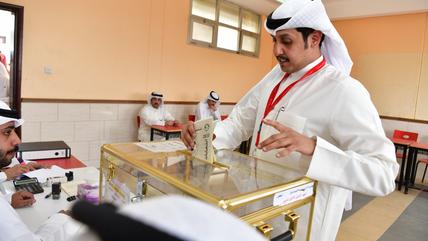 A man wearing a white robe puts a slip of paper into a ballot box.