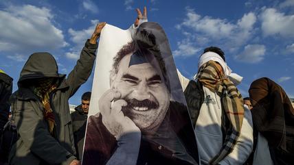 Two hidden youngsters hold poster with face of a smiling man 