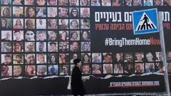 A woman walks past a billboard showing photos of hostages taken by Hamas on 7 October and featuring the hashtag #BringThemHomeNow