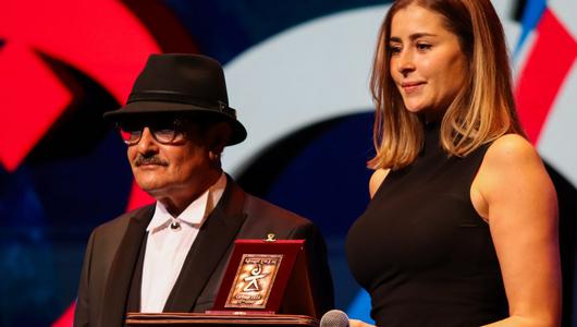 A man in a black hat and a woman stand behind a podium. She is holding a microphone.